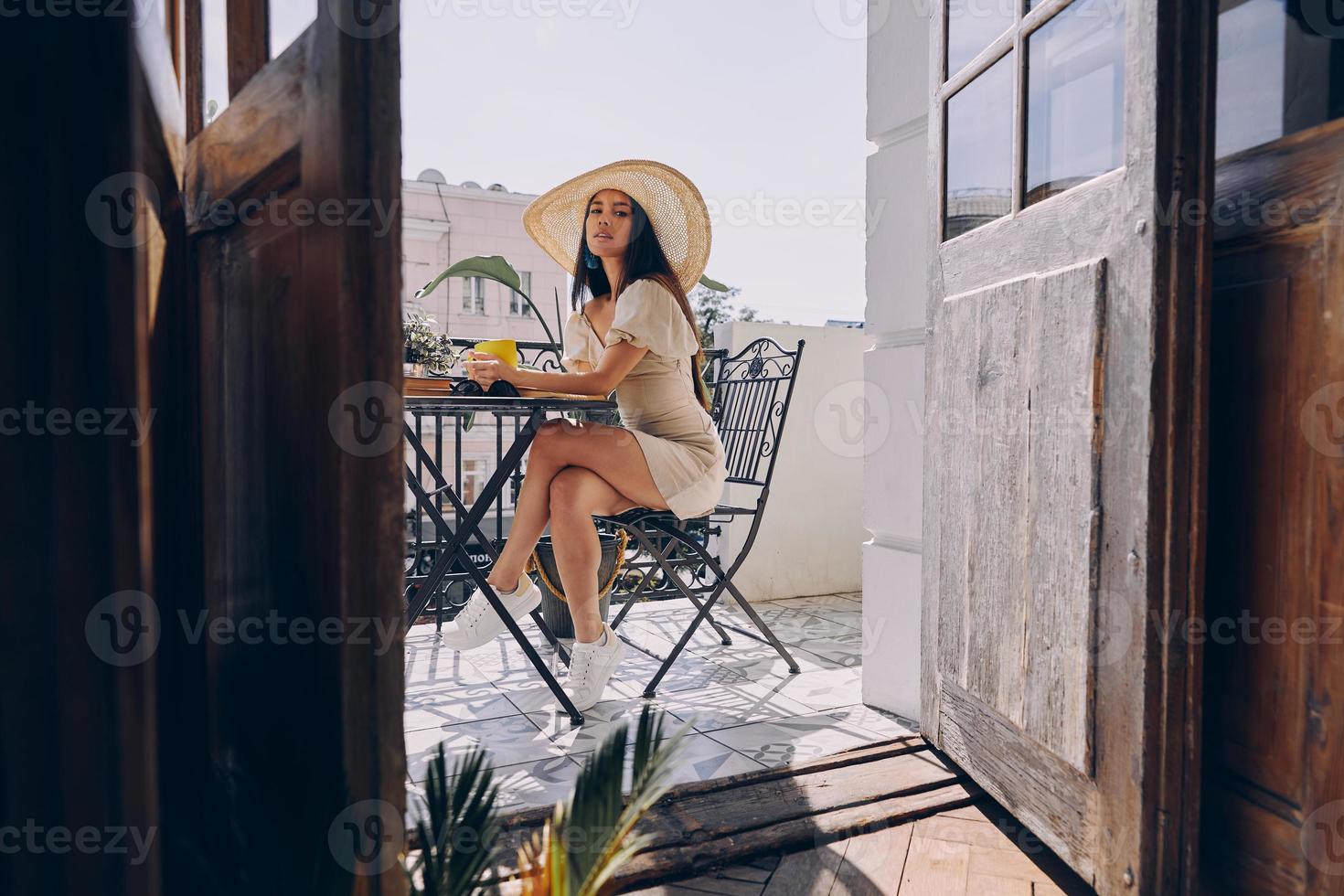 bella joven con elegante sombrero disfrutando de una bebida caliente mientras se relaja en el balcón foto