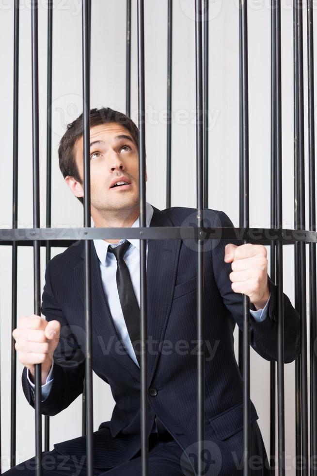 I am not guilty Terrified young man in formalwear standing behind a prison cell and looking up photo