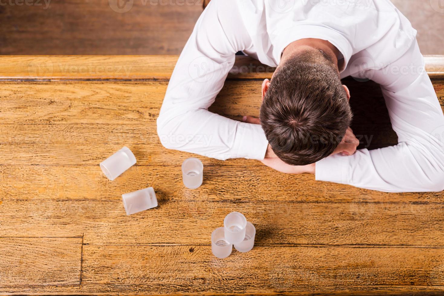This is too much Top view of drunk man in white shirt leaning at the bar counter while empty glasses standing near him photo