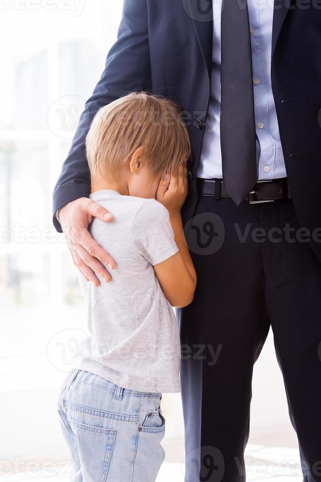 I will be missing you Little boy crying and covering face with hands while his father in formalwear consoling him photo
