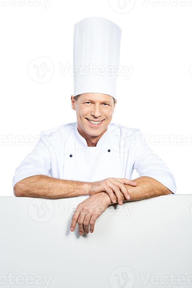Advertising your product. Confident mature chef in white uniform leaning at the copy space while standing against white background photo