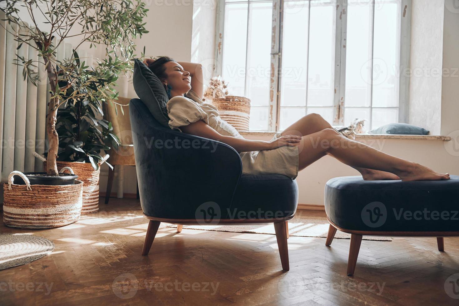 hermosa joven manteniendo los ojos cerrados mientras se relaja en una silla cómoda en casa foto