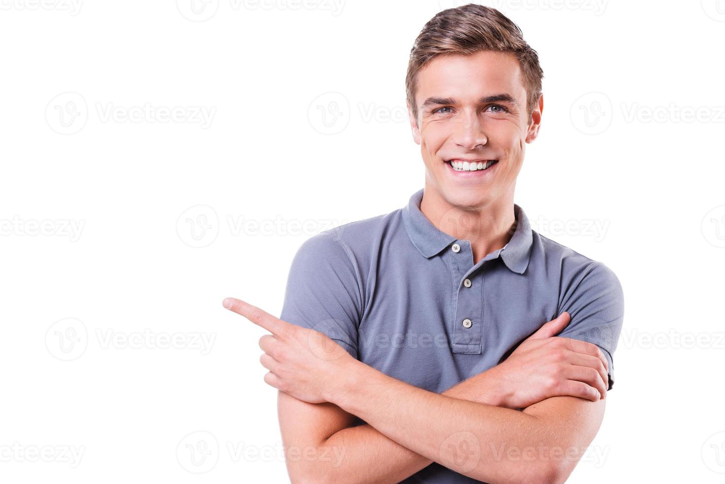 Look at this Handsome young man pointing away and smiling while standing isolated on white background photo