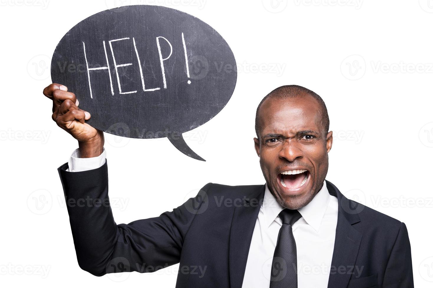 I need help Furious young African man in formalwear holding banner with help text while standing isolated on white background photo
