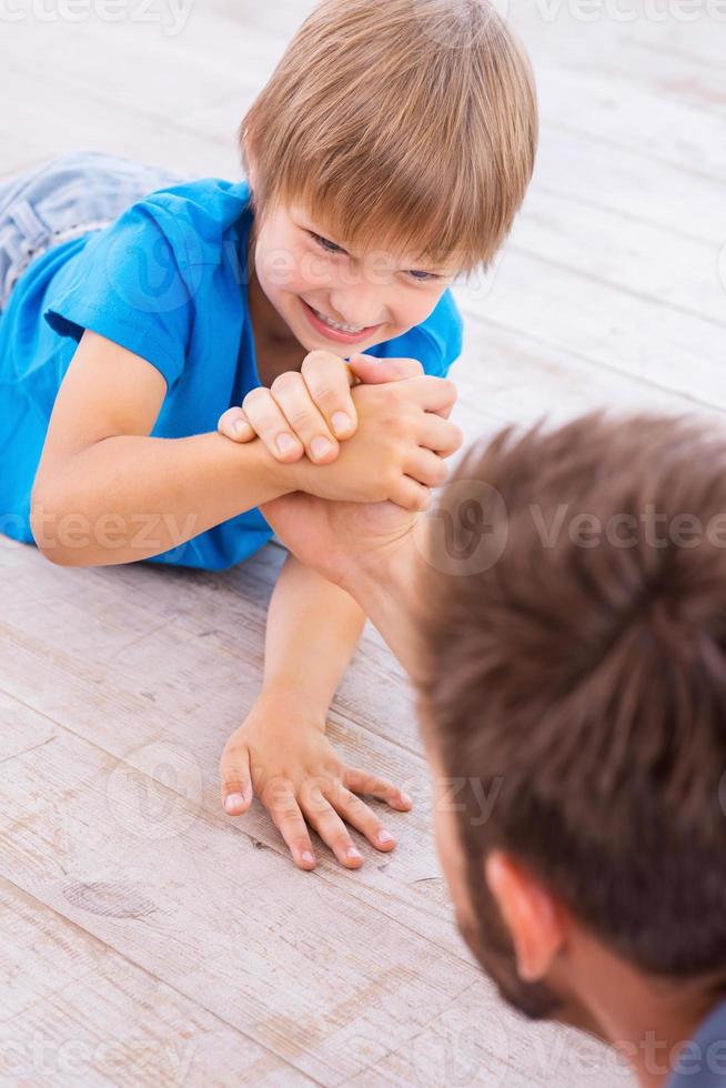 I am winning Top view of father and son competing in arm wrestling while both lying on the hardwood floor photo