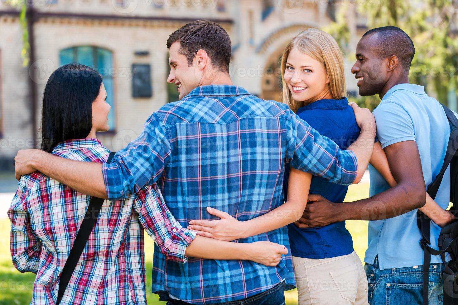 We are the best friends Rear view of beautiful young woman looking over shoulder and smiling while walking together with friends photo