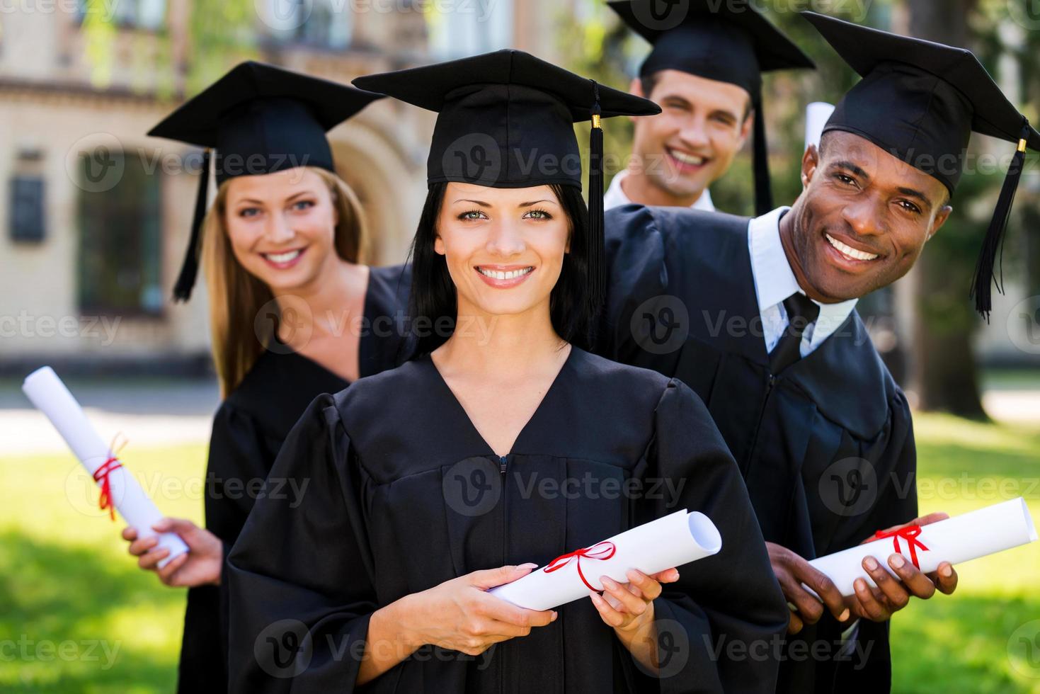 Finally graduated Four college graduates holding diplomas and smiling while standing in a row photo