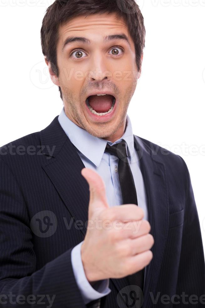 Thumb up for success Happy young man in formalwear showing his thumb up and keeping mouth open while standing isolated on white background photo