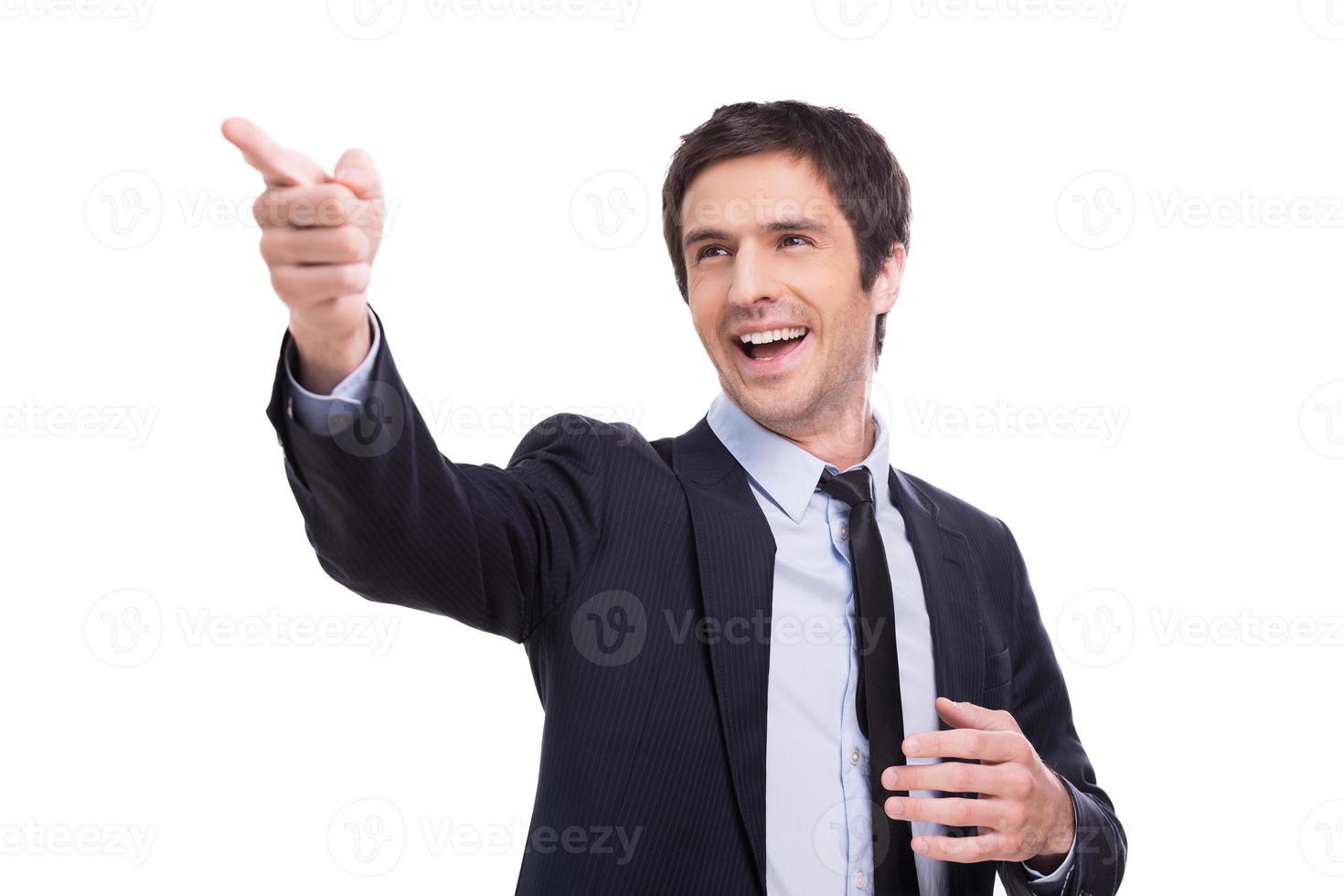 Look at that Happy young man in formalwear pointing away and smiling while standing isolated on white background photo