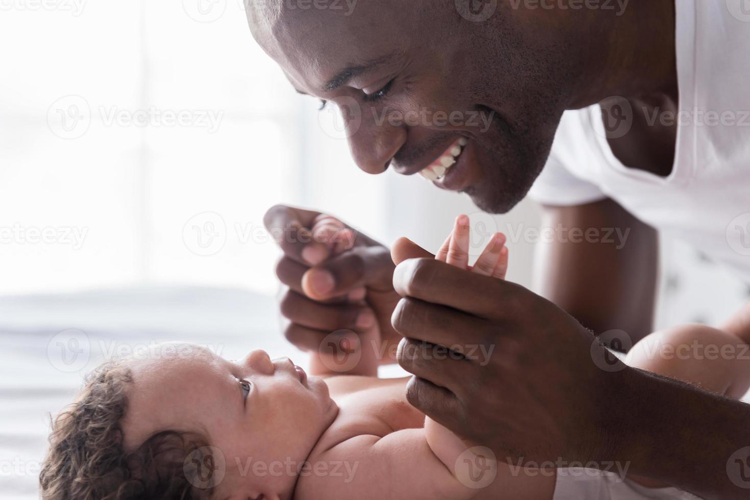 You are my world Side view of happy young African man playing with his little baby and smiling while lying in bed photo