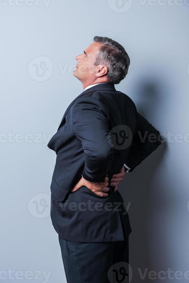 Good idea Thoughtful mature man in formalwear pointing up while standing against grey background photo