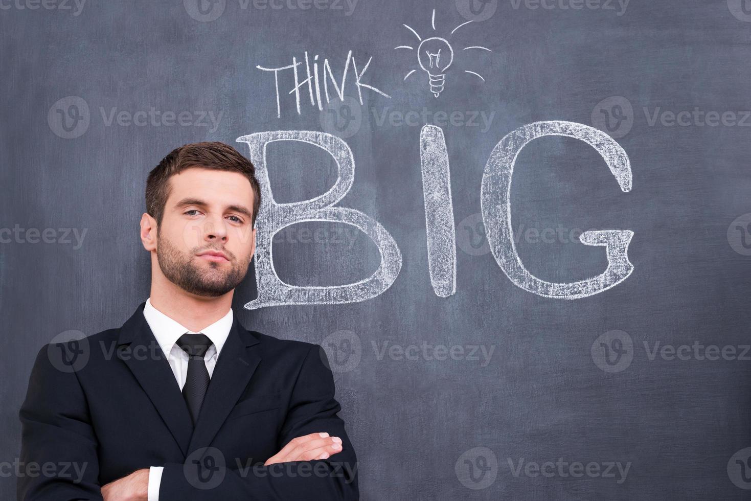 Turn your brains on Portrait of young businessman keeping arms crossed and looking at camera standing against chalk drawing on the blackboard photo