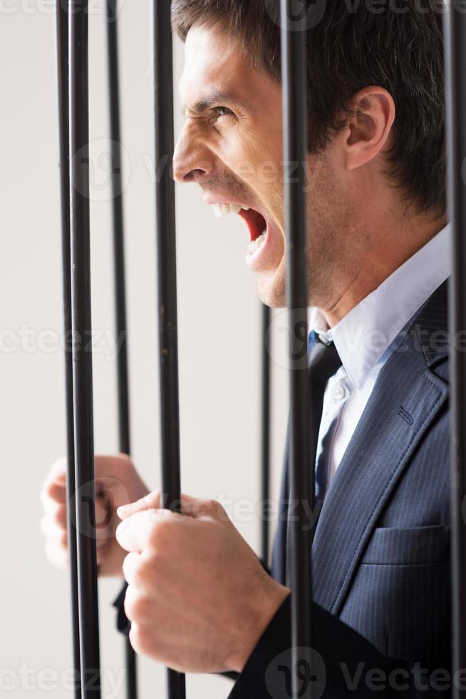 Let me free Side view of furious young man in formalwear standing behind a prison cell and shouting photo