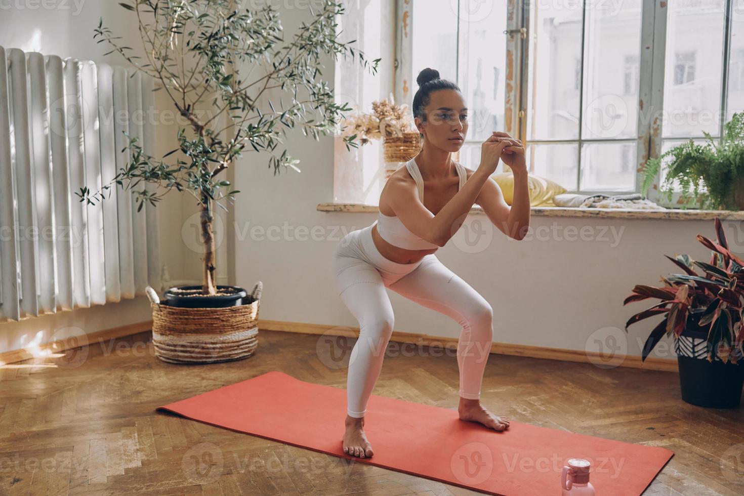 Beautiful woman standing in squatting position while practicing in front of the window at home photo