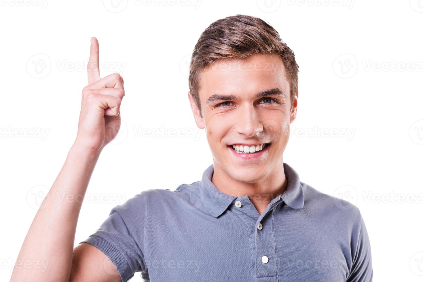 Look over there Handsome young man pointing up and smiling while standing isolated on white background photo