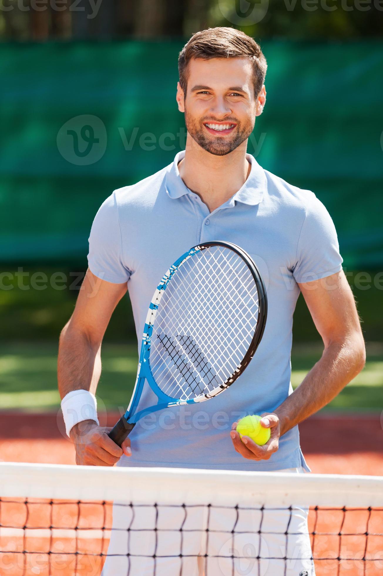 Tennis is my life Happy young man in polo shirt holding tennis racket and ball while standing on tennis court 13692643 Stock Photo at Vecteezy