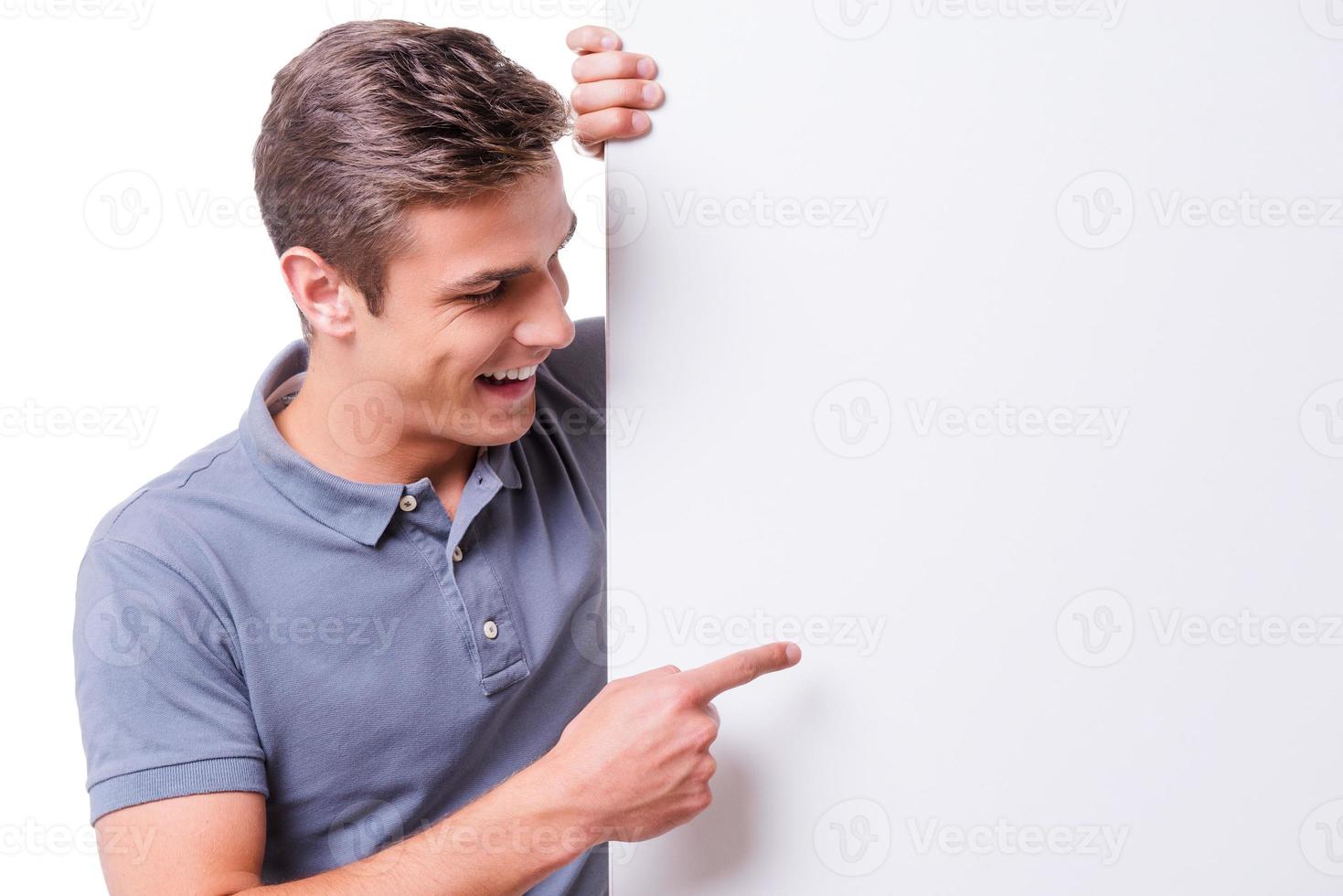 Look at that Happy young man pointing copy space and smiling while standing against white background photo