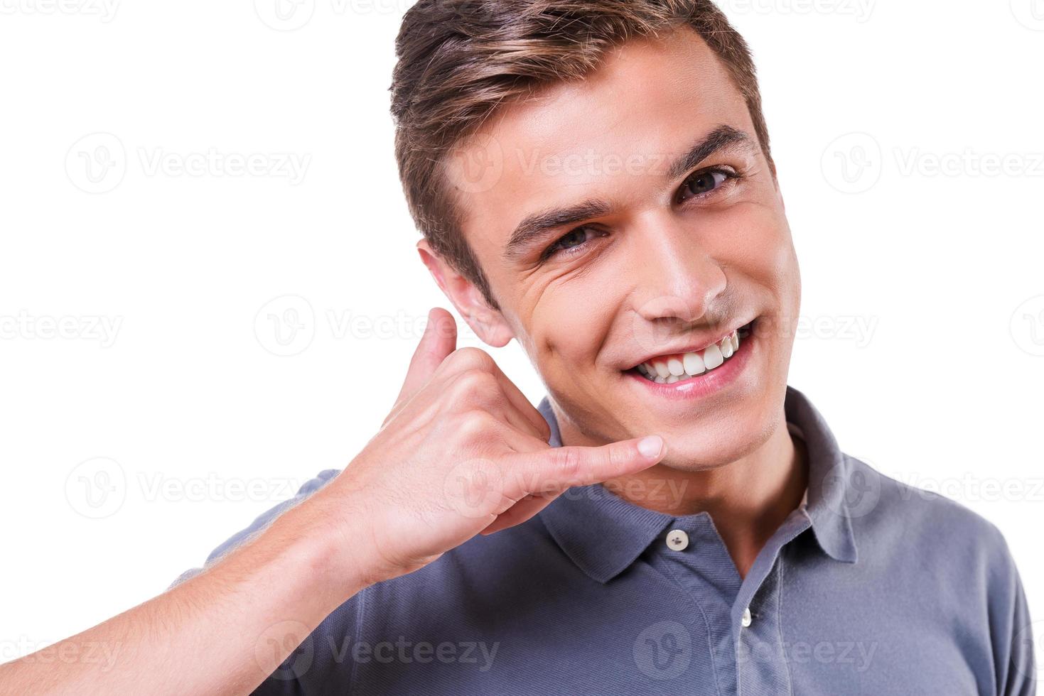 Call me Happy young man gesturing mobile phone near face and smiling while standing isolated on white background photo