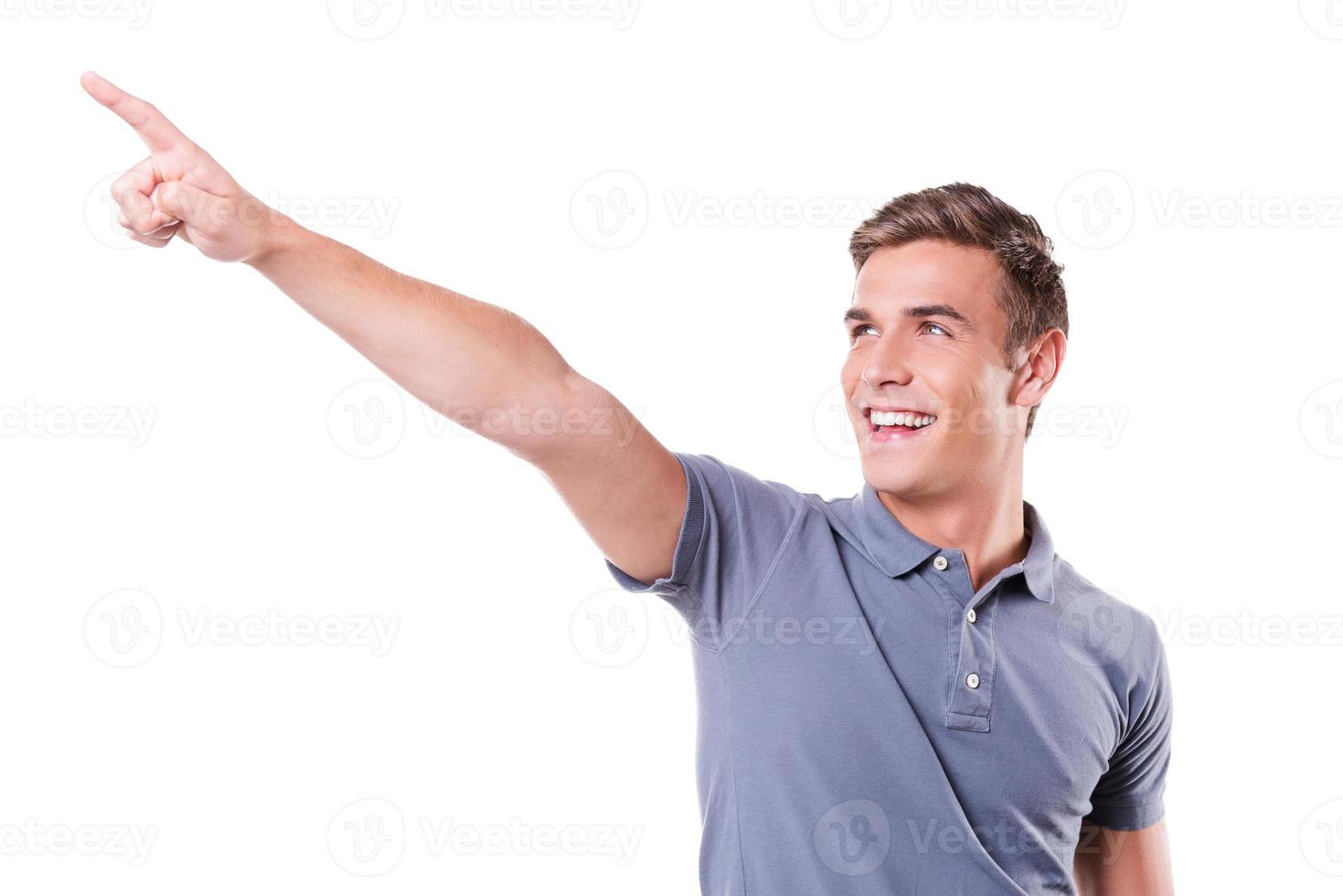 What is there Handsome young man pointing away and smiling while standing isolated on white background photo