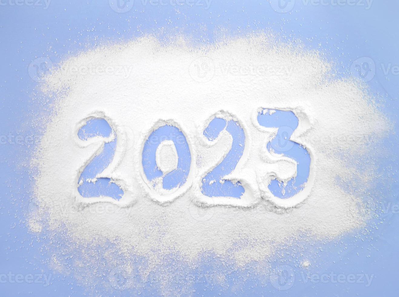 Christmas background with snow. 2023 is written on a white powder on a blue background. Powdered sugar new year photo