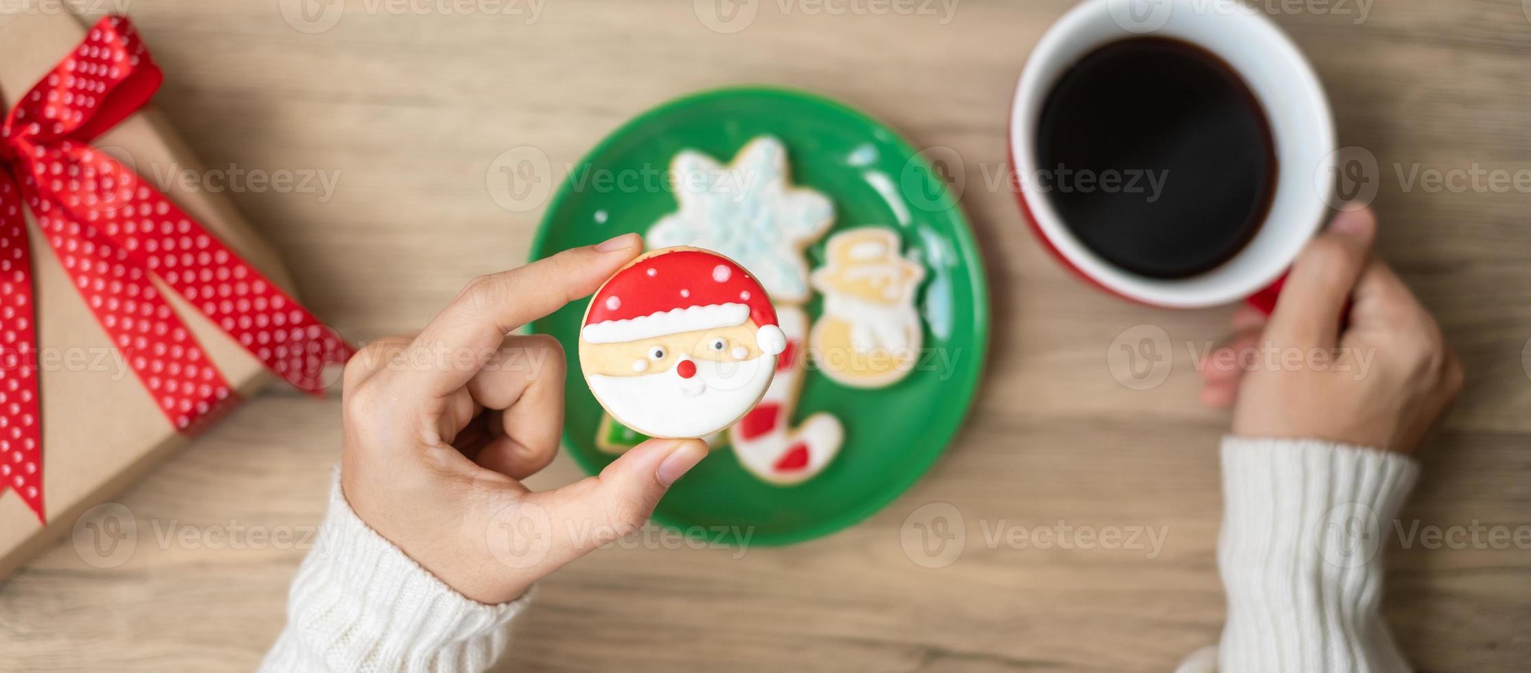 Merry Christmas with woman hand holding coffee cup and homemade cookie on table. Xmas eve, party, holiday and happy New Year concept photo