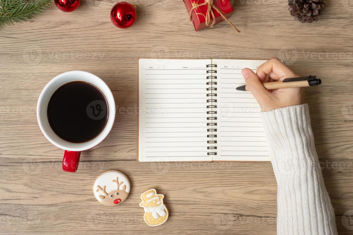 Woman hand writing on notebook with black coffee cup and Christmas cookies on table. Xmas, Happy New Year, Goals, Resolution, To do list, Strategy and Plan concept photo