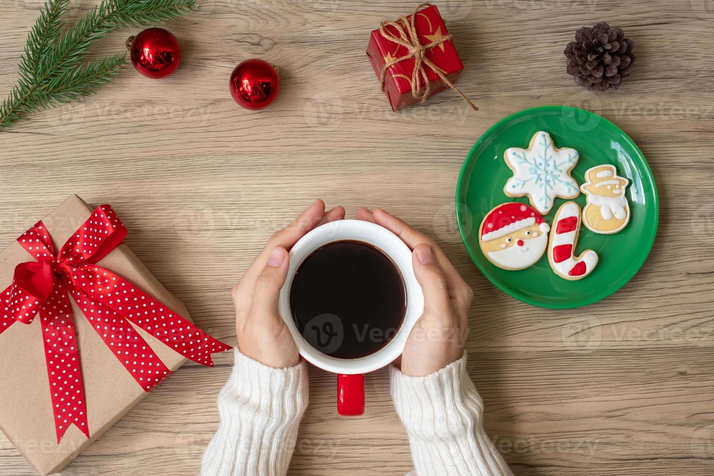 feliz navidad con la mano de una mujer sosteniendo una taza de café y una galleta casera en la mesa. concepto de víspera de navidad, fiesta, vacaciones y feliz año nuevo foto
