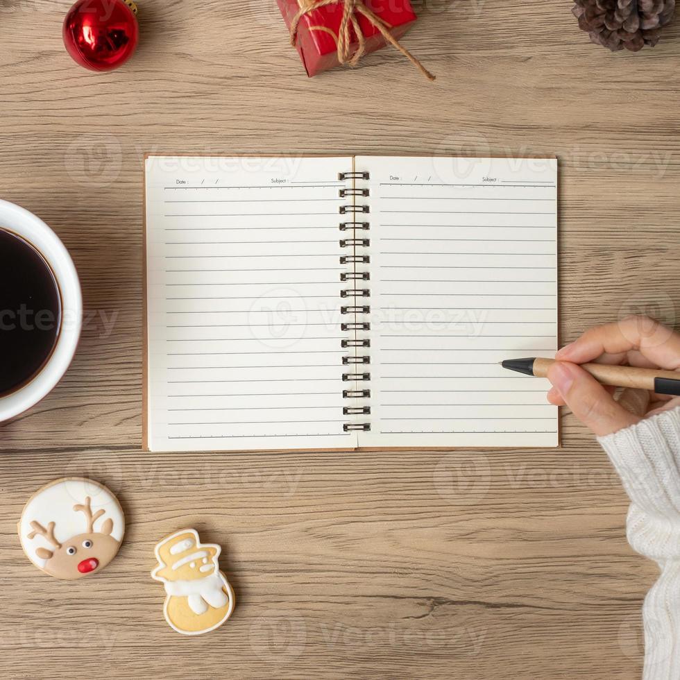 Woman hand writing on notebook with black coffee cup and Christmas cookies on table. Xmas, Happy New Year, Goals, Resolution, To do list, Strategy and Plan concept photo