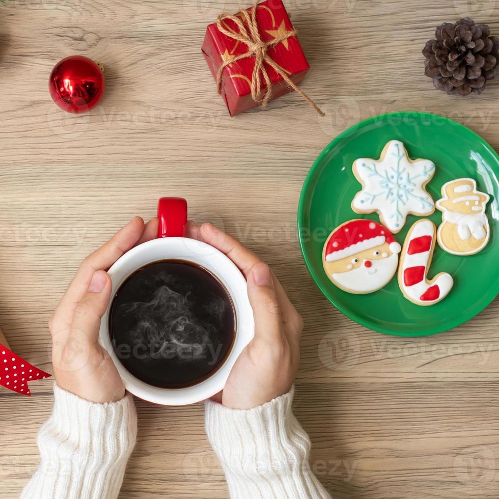Merry Christmas with woman hand holding coffee cup and homemade cookie on table. Xmas eve, party, holiday and happy New Year concept photo