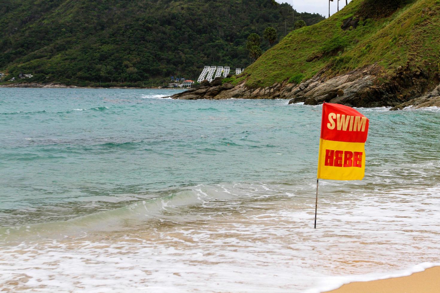 Red with yellow swim hear flag on the beach and sea to tell or inform traveler , tourist and people can swimming in this area at Phuket, Thailand. Seascape with wave, sky and mountain background. photo