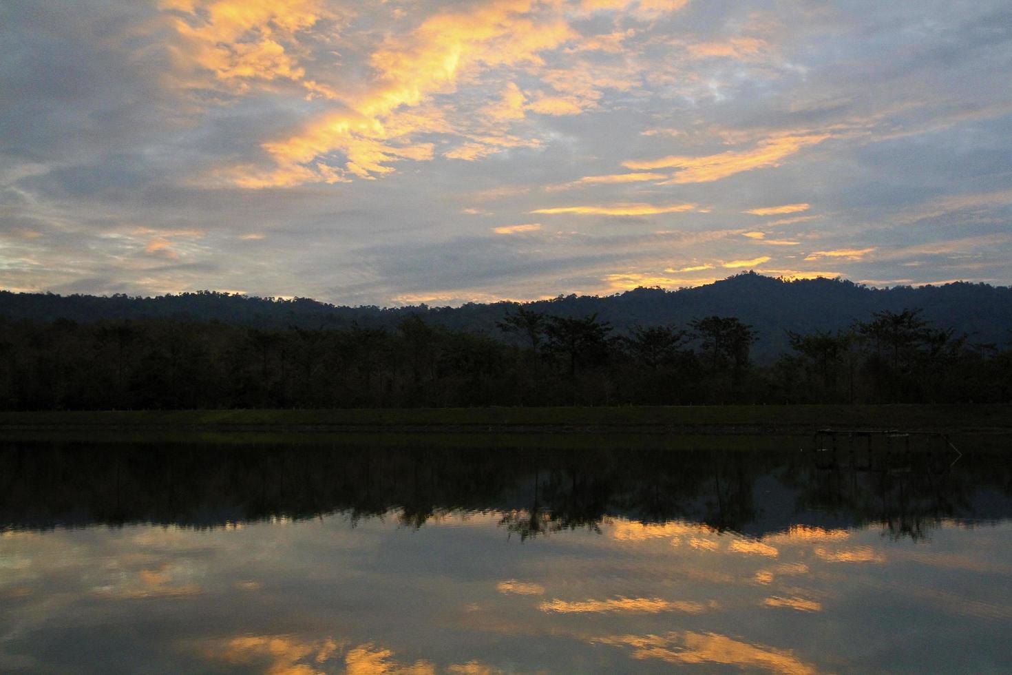 silueta de montaña y reflejo de nube en lago o río con fondo de bosque y cielo al atardecer o al amanecer. belleza en la naturaleza y papel tapiz natural. foto