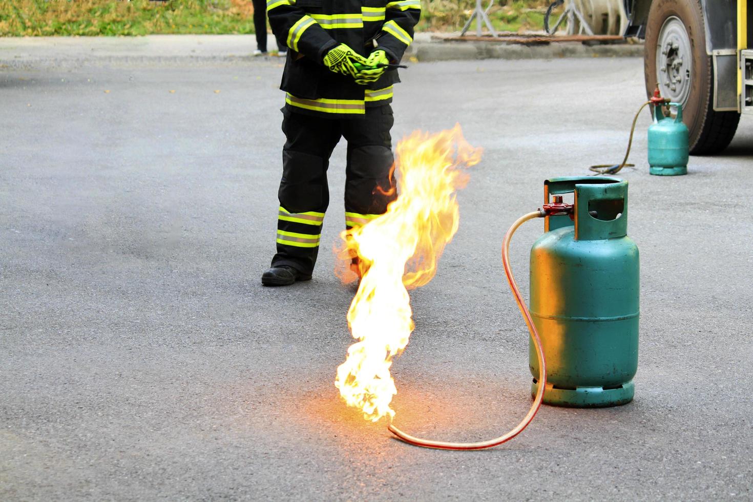 Fire burning on green gas container and Firefighter or fireman in black and green safety uniform or suit and extinguish fire on street with car wheel background and copy space. Conflagration and risk. photo