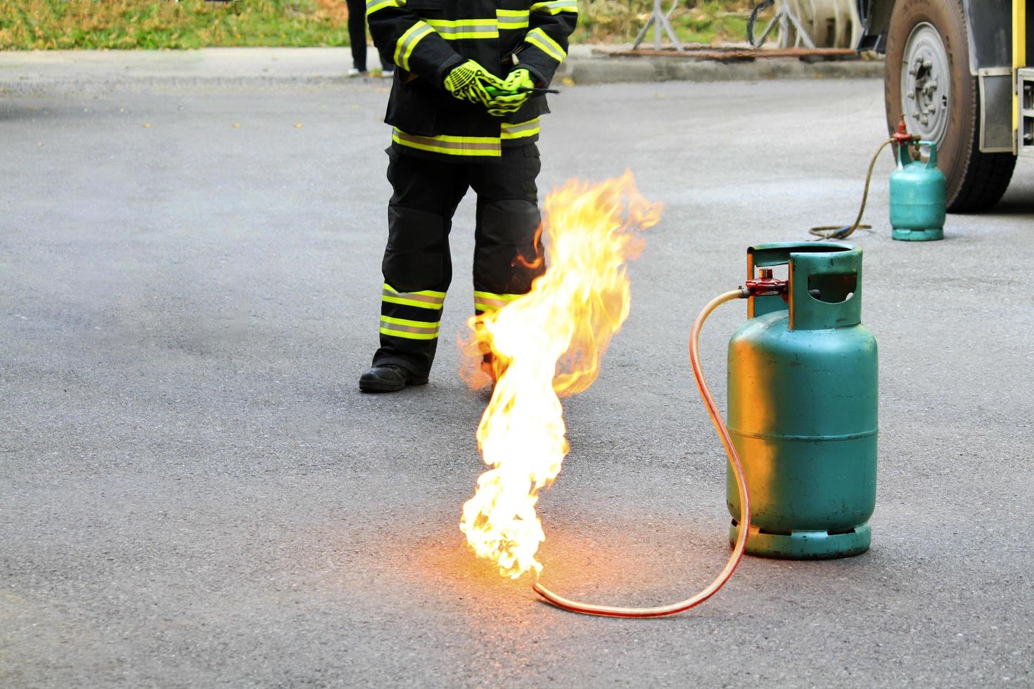 fuego ardiendo en un contenedor de gas verde y bombero o bombero con uniforme de seguridad negro y verde o traje y extinguir el fuego en la calle con fondo de rueda de camión y espacio para copiar. conflagración y riesgo. foto