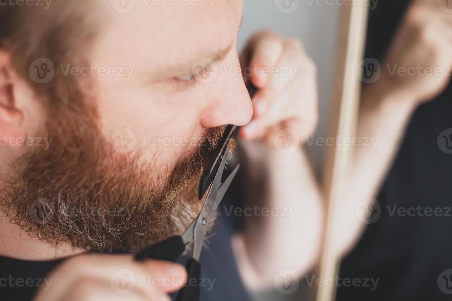 Man cutting moustache and beard himself at home photo