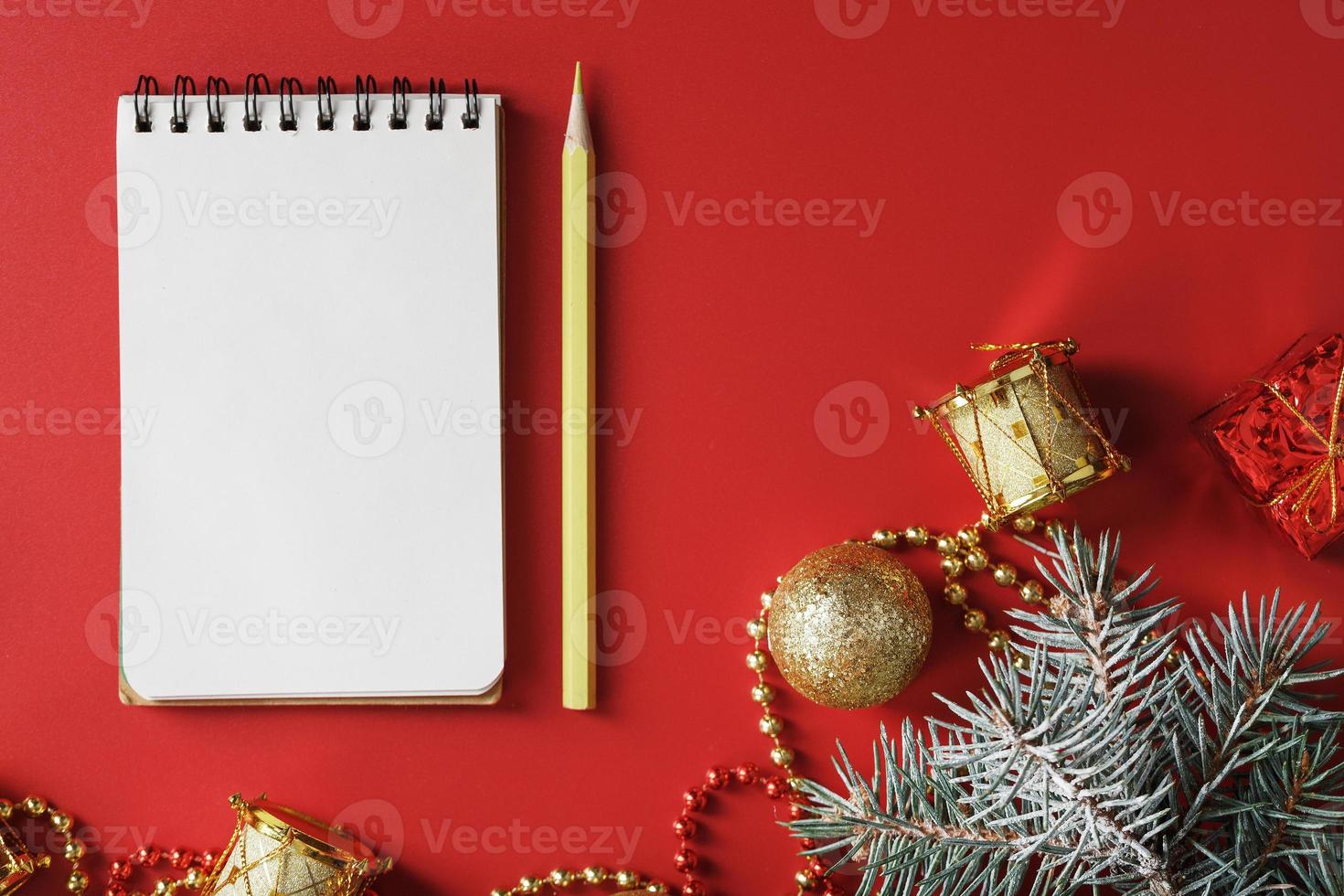 Christmas composition with notepad and a pencil for writing wishes with Christmas tree decorations on a red background. photo