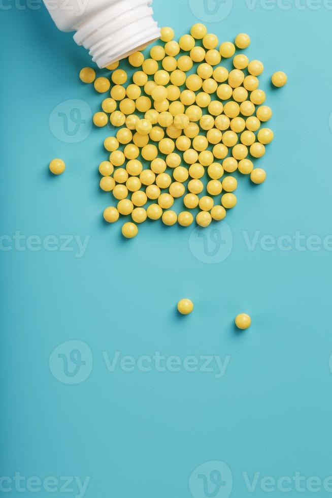 Yellow vitamin C capsules spilled out of a white jar against a blue background. photo