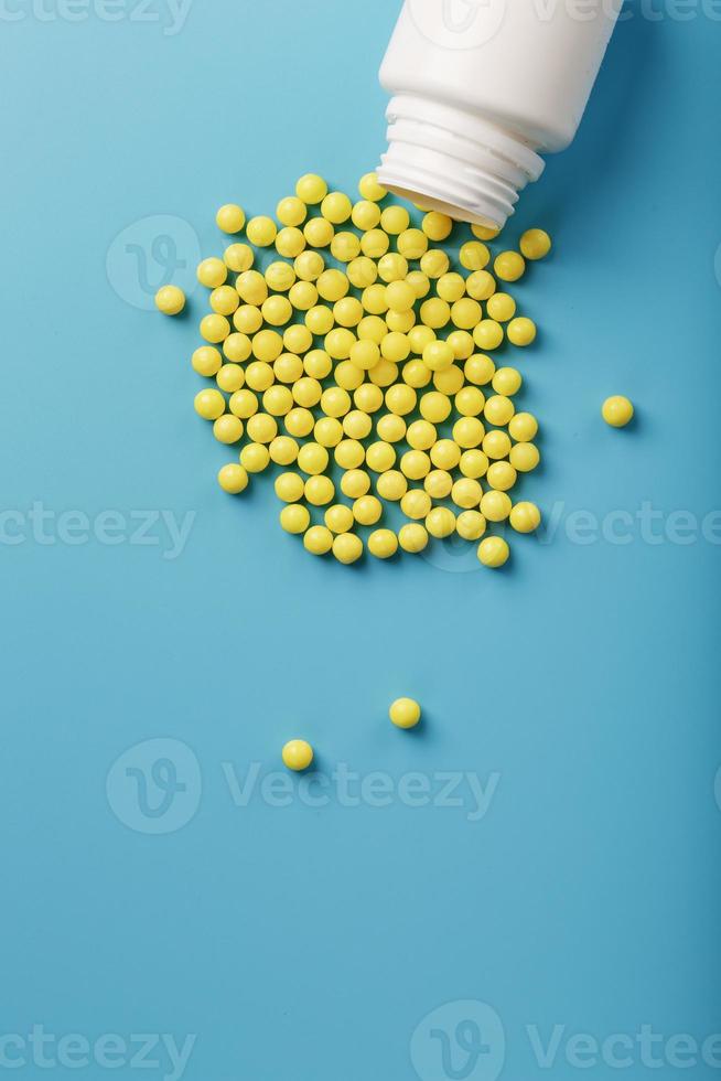 vitaminas amarillas en forma de grageas redondas vertidas del frasco sobre un fondo azul. foto