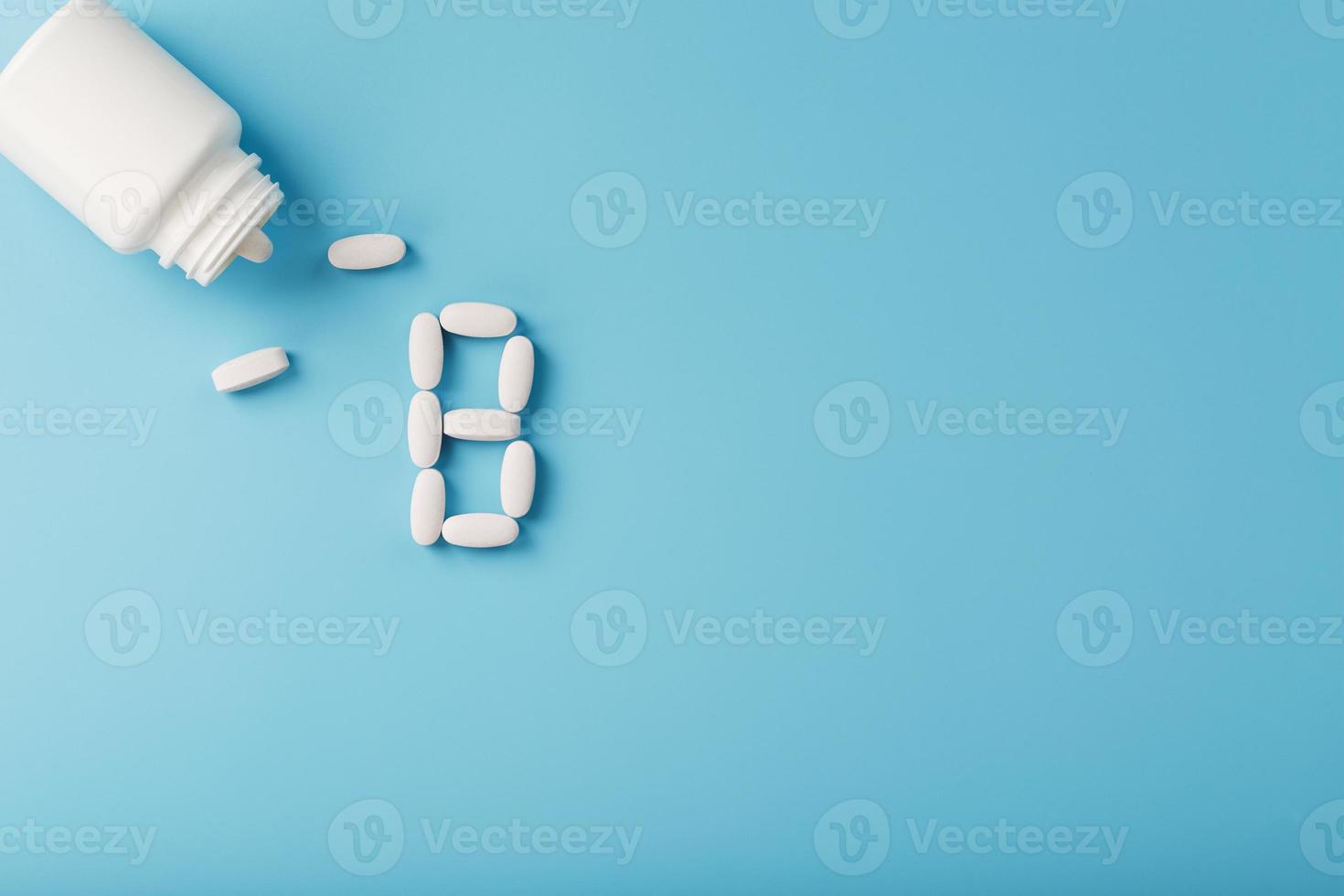 Vitamin B pills fell out of a white jar on a blue background. The letter In the inscription. photo