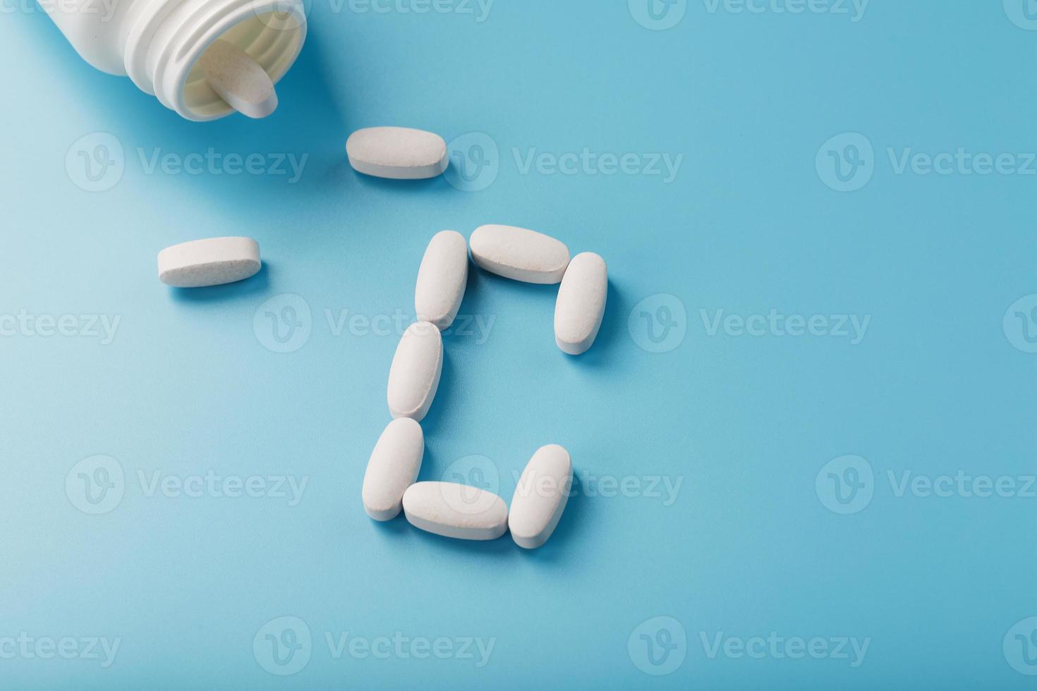 White capsules with vitamins in the form of C are poured from a jar on a blue background. photo