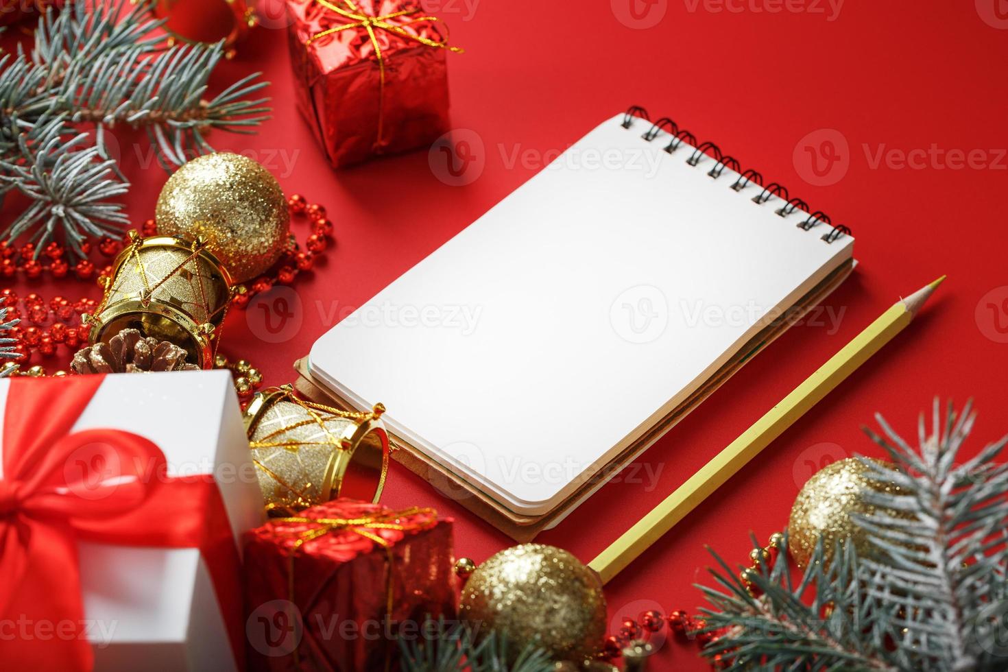 Christmas composition with notepad and a pencil for writing wishes with Christmas tree decorations on a red background. photo