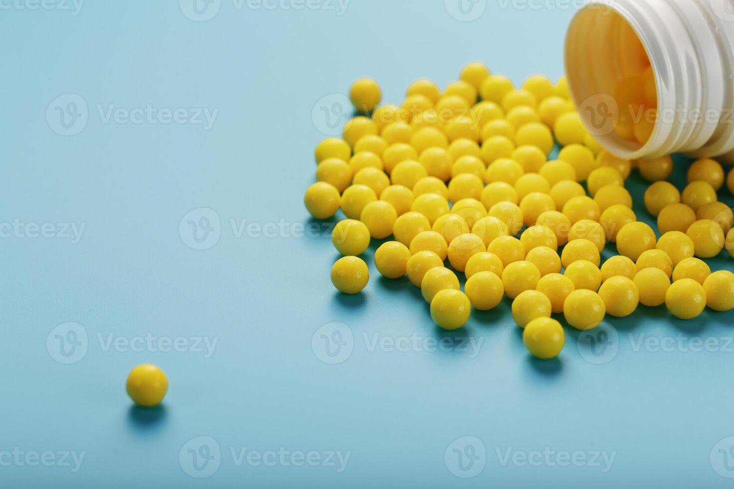 Yellow vitamin C capsules spilled out of a white jar against a blue