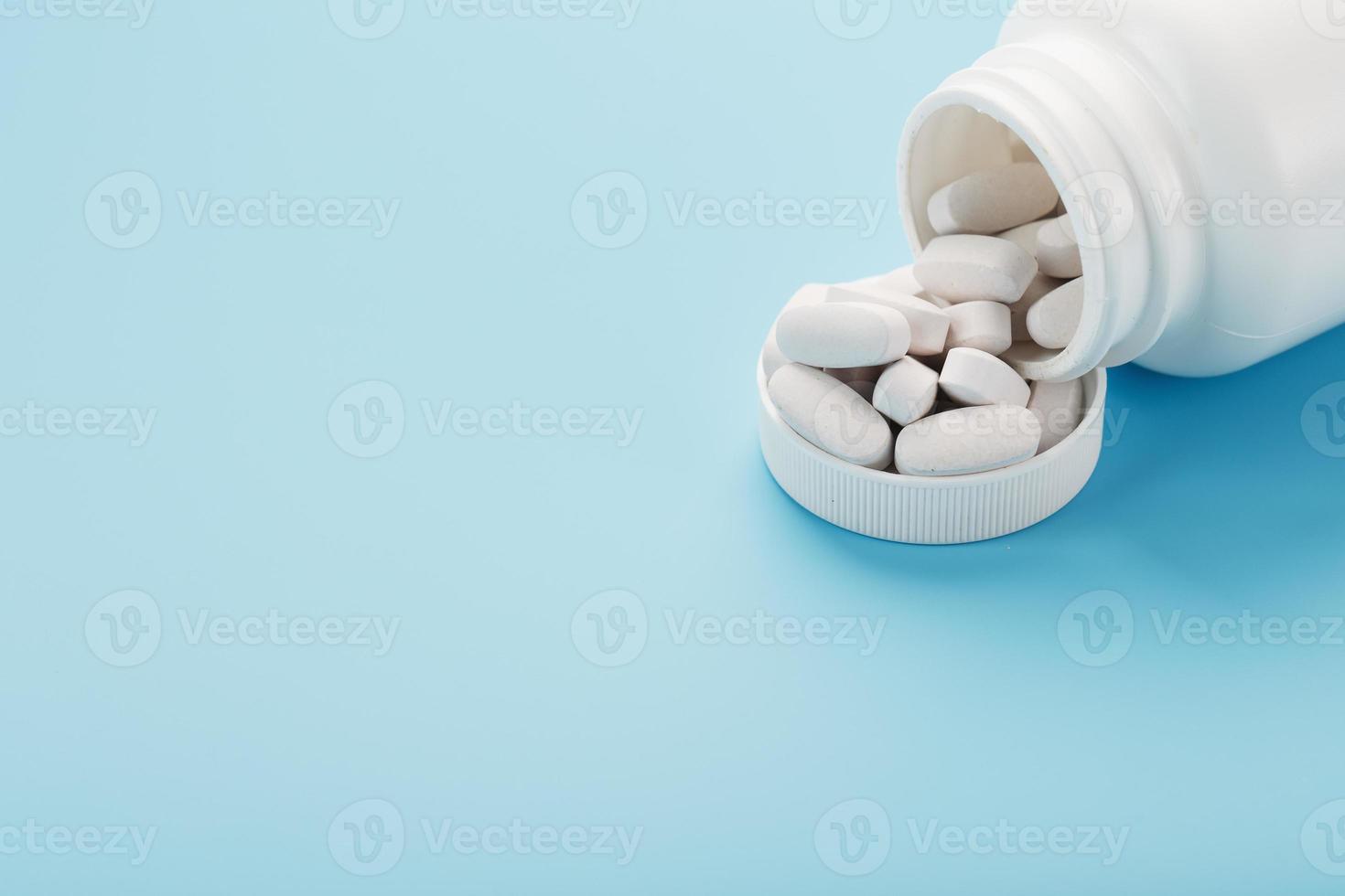 White capsules with vitamins and minerals in the form are poured from a jar on a blue background. photo