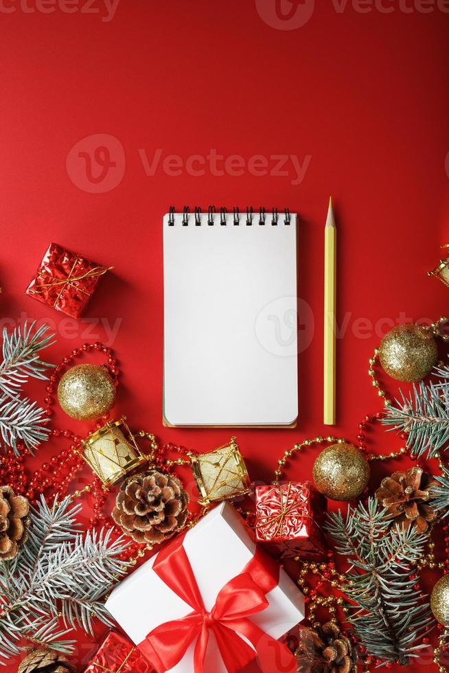 Christmas composition with notepad and a pencil for writing wishes with Christmas tree decorations on a red background. photo
