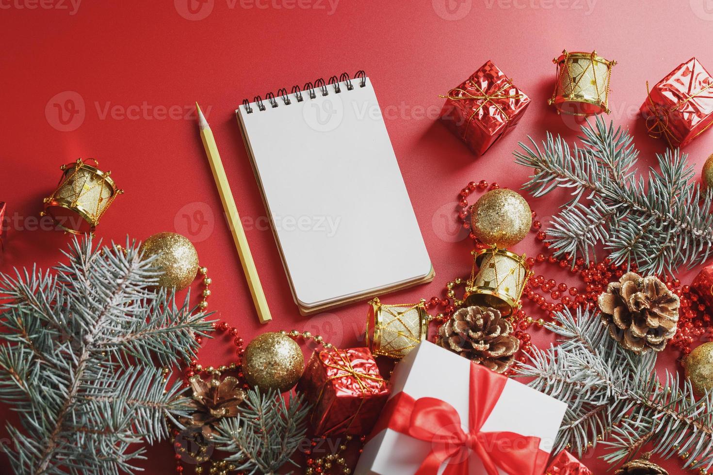 Notepad and pencil for writing wishes and gifts for the New Year and Christmas around the Christmas tree decorations on a red background. photo