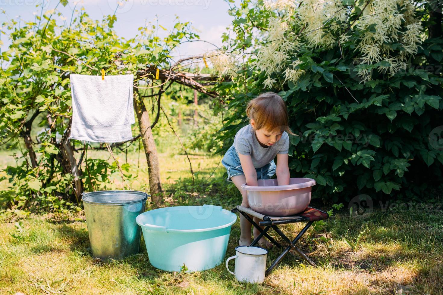 la niña de preescolar ayuda con la lavandería. niño lava ropa en el jardín foto