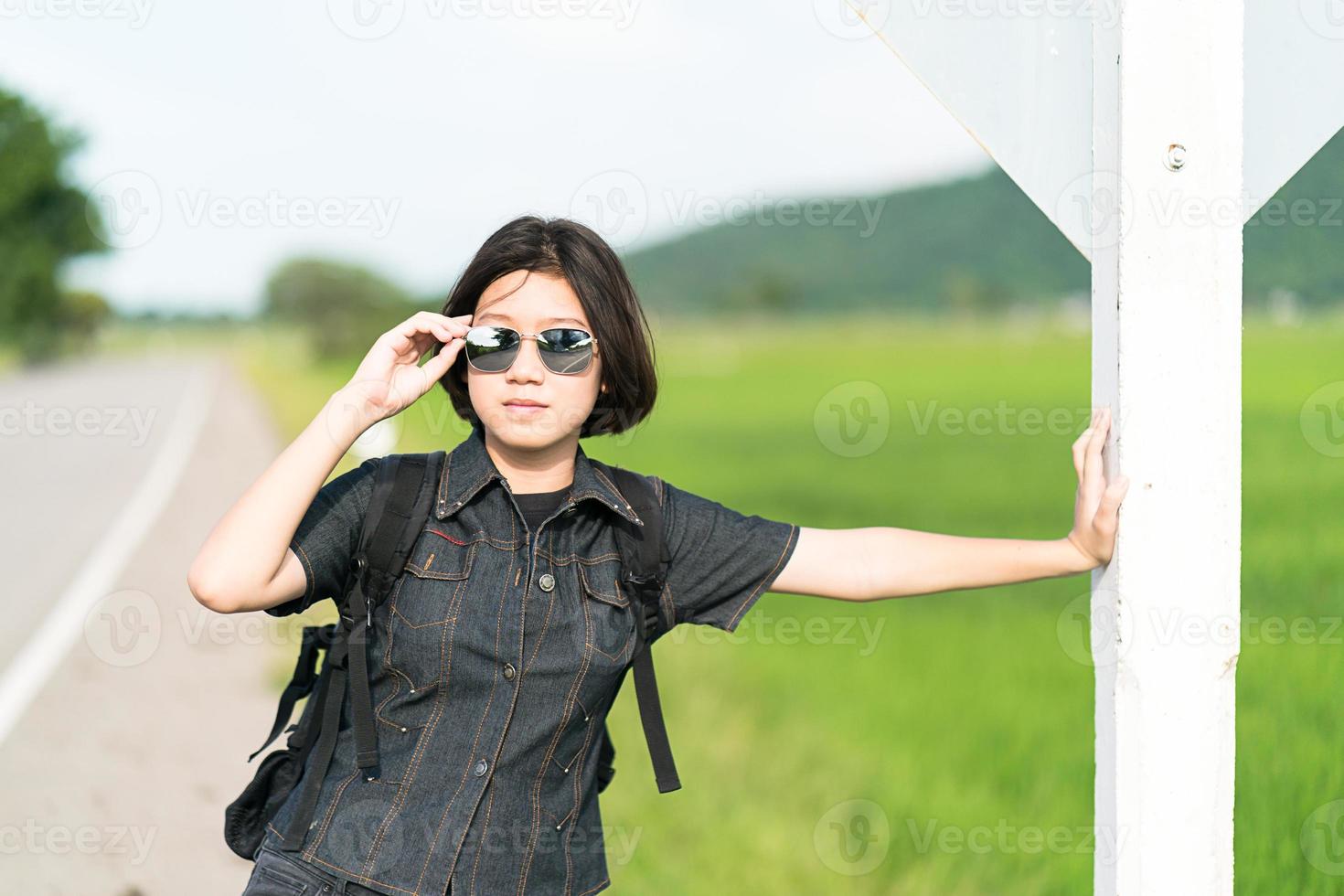Woman stand with backpack hitchhiking along a road photo