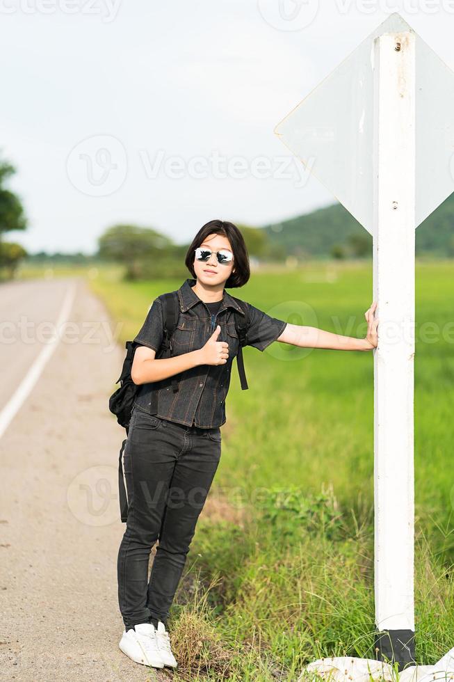 Woman stand with backpack hitchhiking along a road photo