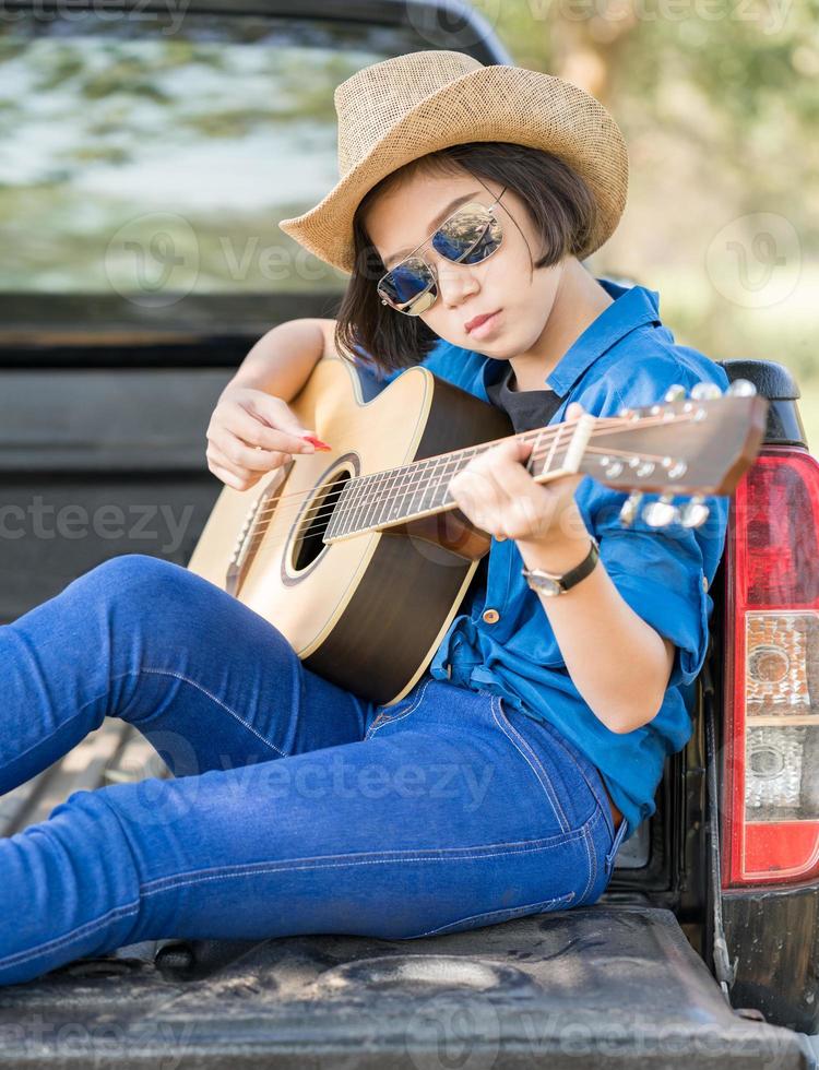 Woman wear hat and playing guitar on pickup truck photo
