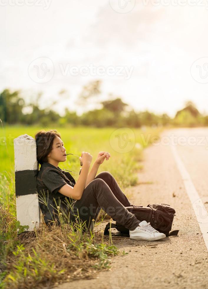 Woman sit with backpack hitchhiking along a road in countryside photo