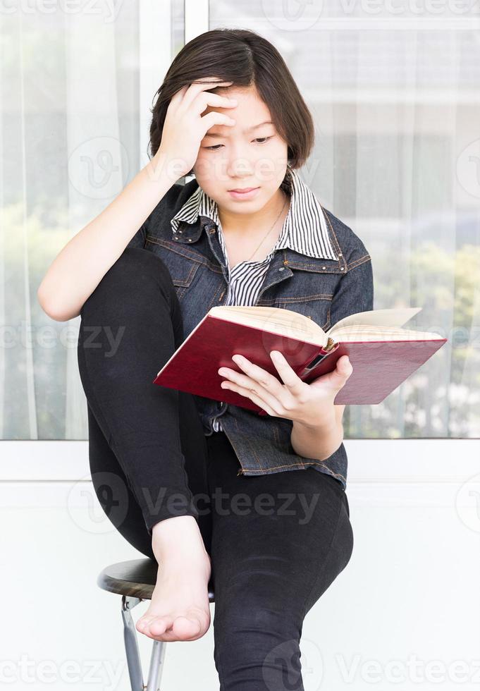 Young woman reading book sitting on chair photo